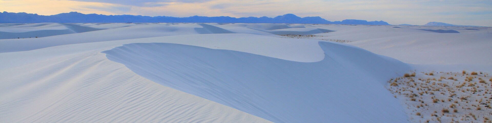 Un extenso paisaje desértico con dunas de arena ondulantes bajo un cielo parcialmente nublado.