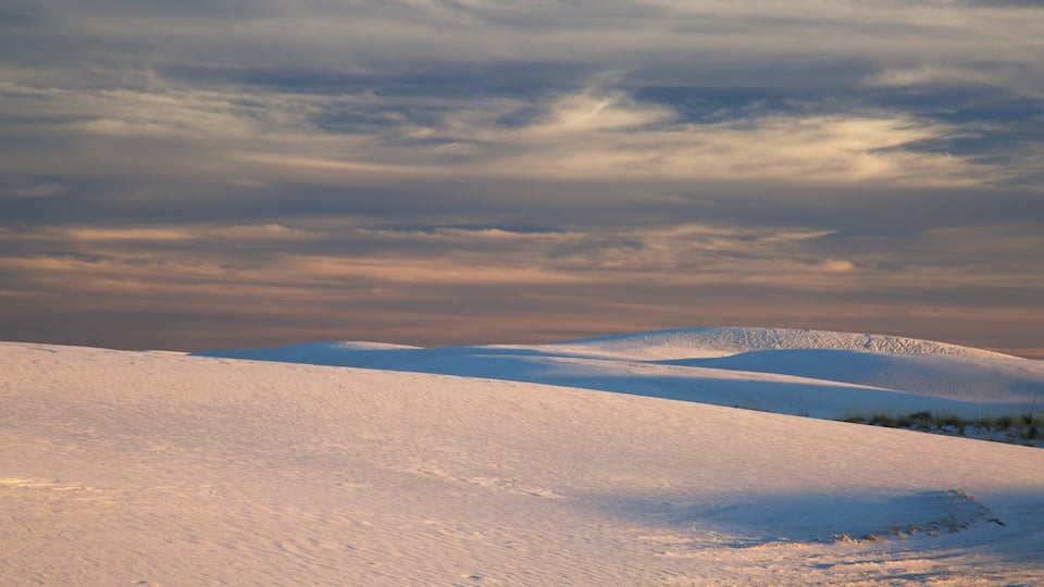 A snow-covered landscape with rolling hills and a cloudy sky.