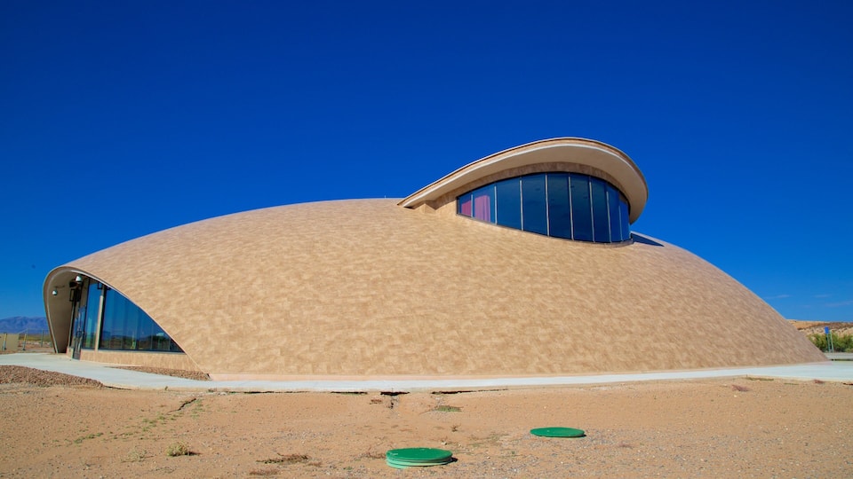 A modern, dome-shaped building with a curved roof and large windows, set against a clear blue sky and desert landscape.