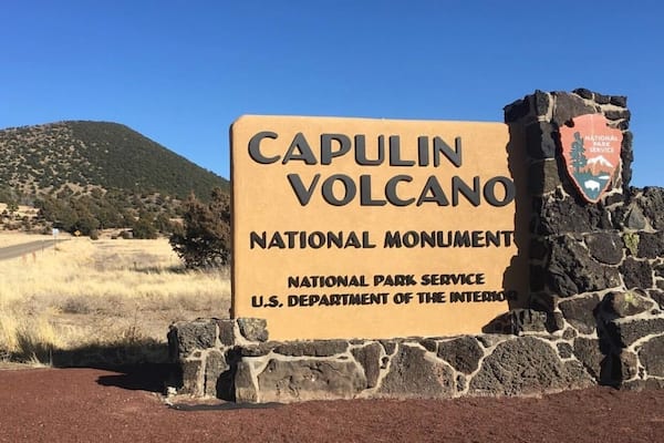 A sign for Capulin Volcano National Monument with a clear sky and a mountain in the background.