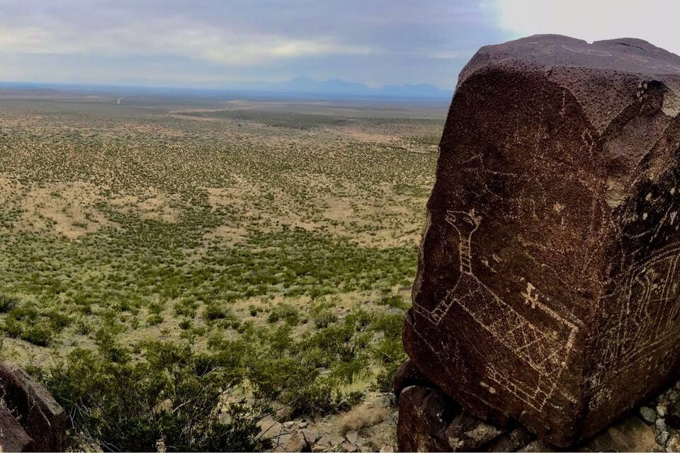 Un masso imponente con intagli, circondato da vegetazione rada in un paesaggio desertico.