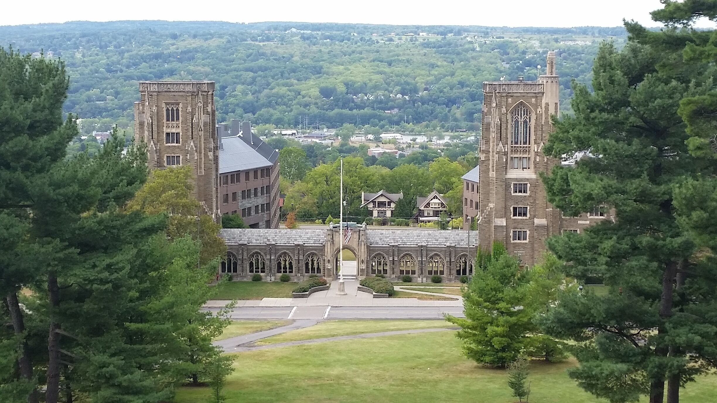 A large, historic building with two tall towers and a central archway, surrounded by lush green trees.