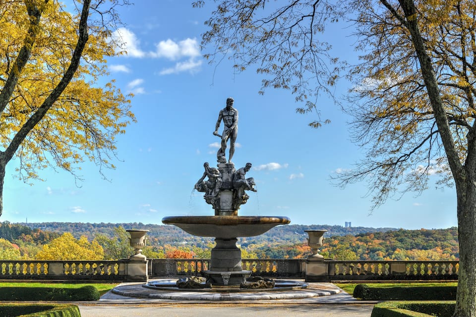 Een klassieke fontein met een standbeeld in een park met herfstkleuren.
