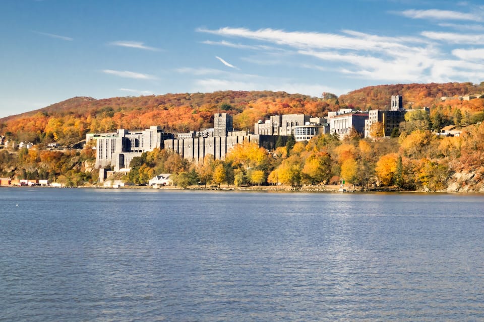 A lakeside cityscape with autumn foliage, historic buildings, and a hill in the background.