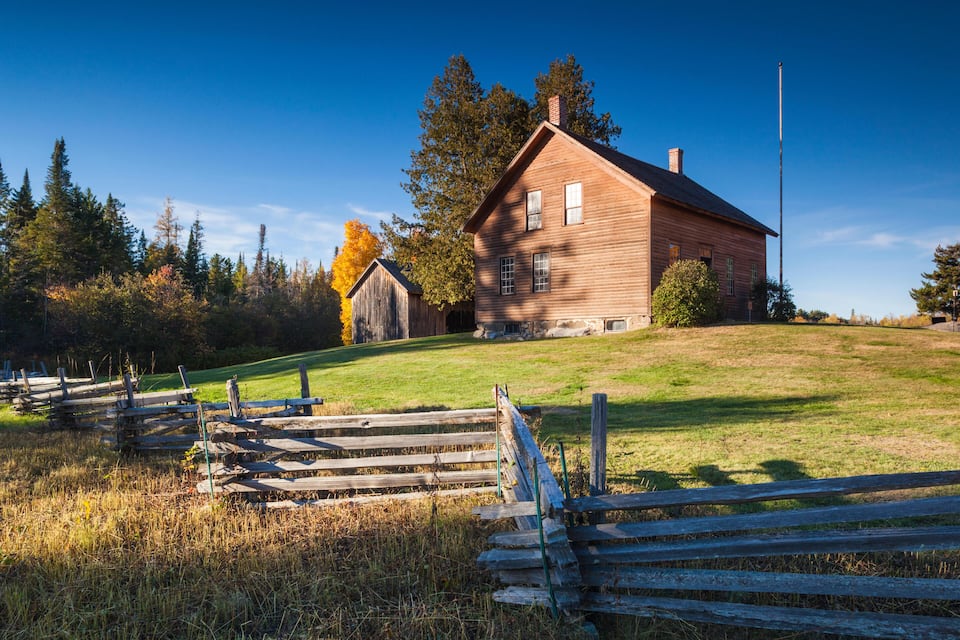 A wooden house on a grassy hill with a wooden fence in the foreground.