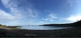 Eine Küstenlandschaft mit Sandstrand, ruhigem Wasser und einem bewaldeten Hügel im Hintergrund.