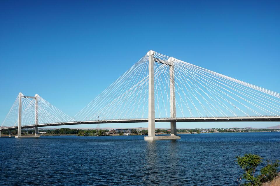 Un puente colgante imponente que cruza un río ancho bajo cielos azules y despejados.