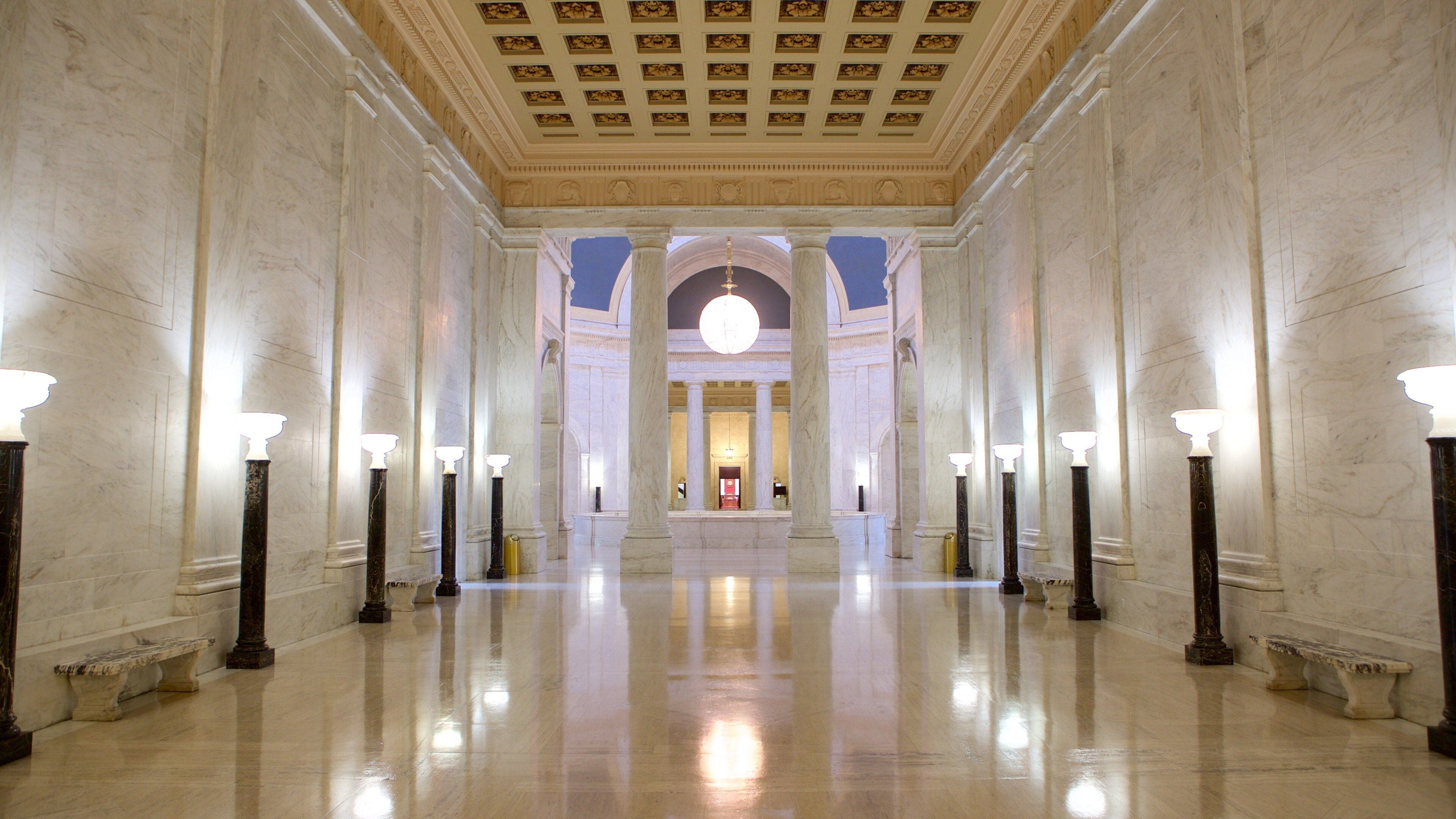 A grand hallway with marble walls, columns, and a large chandelier.