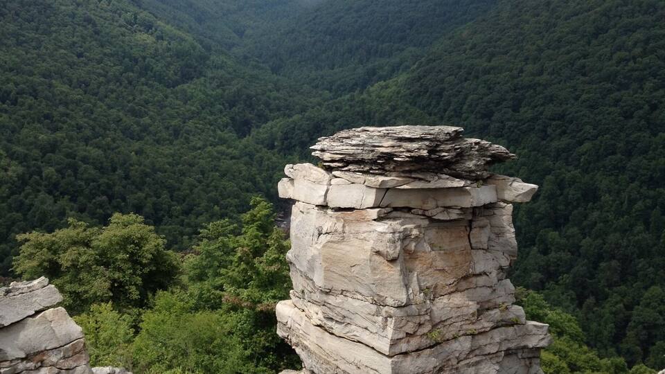 A rocky outcrop with a layered rock formation surrounded by dense forest and rolling hills.