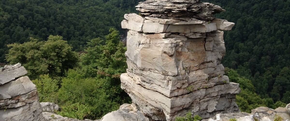 A rocky outcrop with a layered rock formation surrounded by dense forest and rolling hills.
