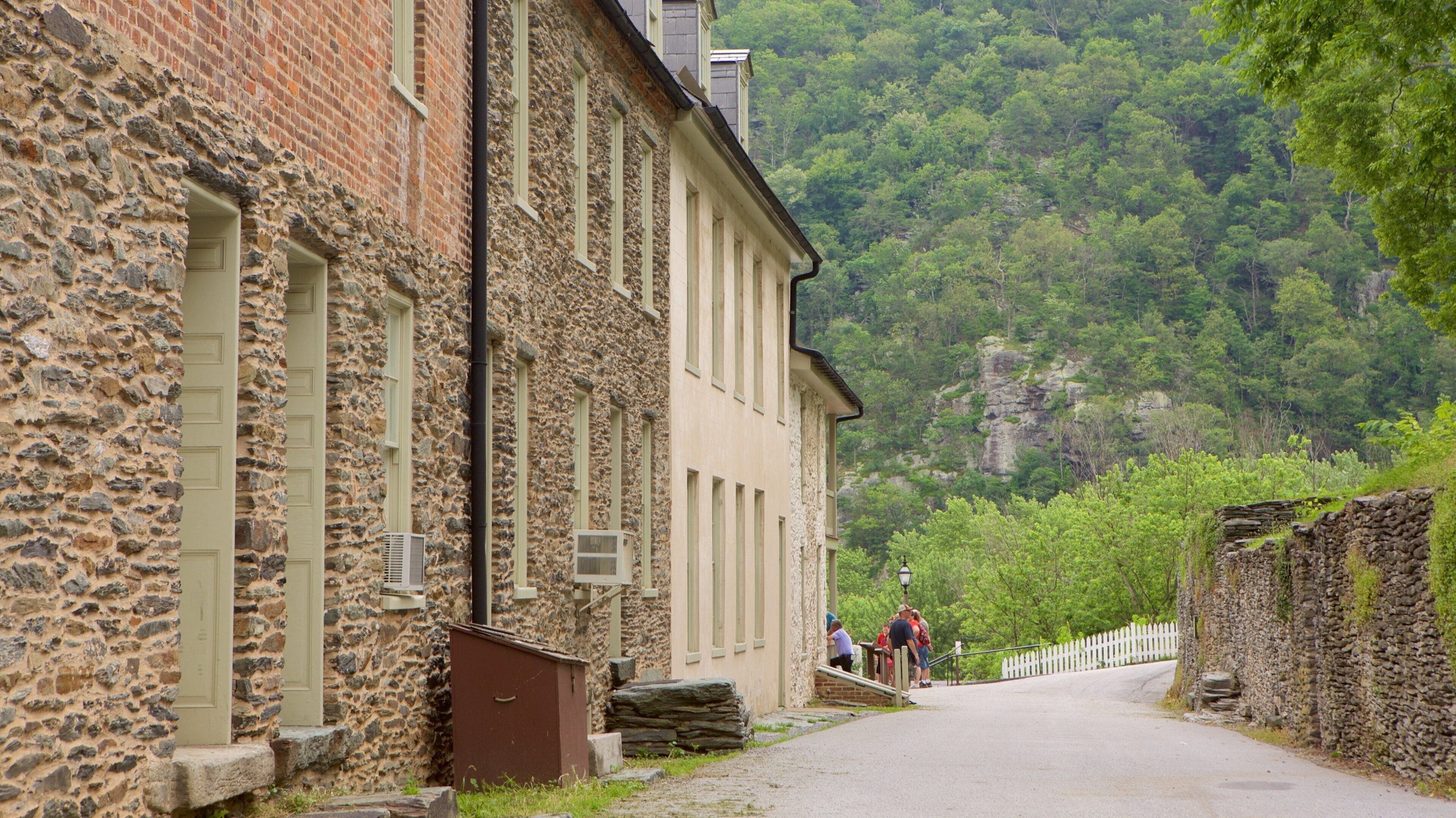 A stone building with a paved path leading to a white picket fence.