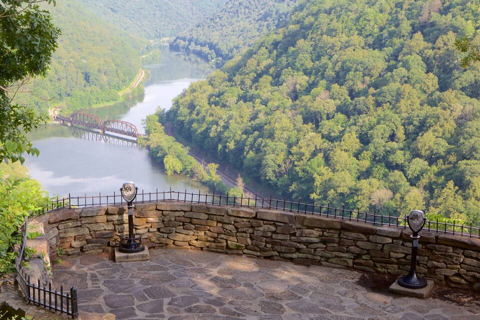 A stone viewing platform overlooking a river with a bridge, surrounded by dense forest.