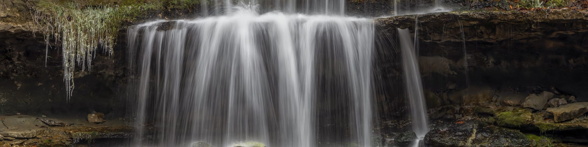 A multi-tiered waterfall cascading over rocky terrain surrounded by autumn foliage.