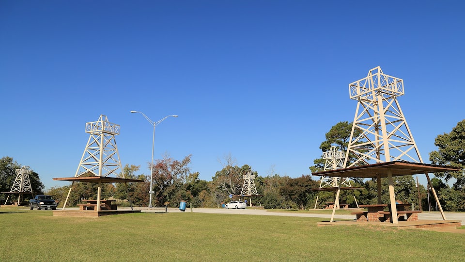 Two large metal structures resembling power pylons in a park with picnic tables.