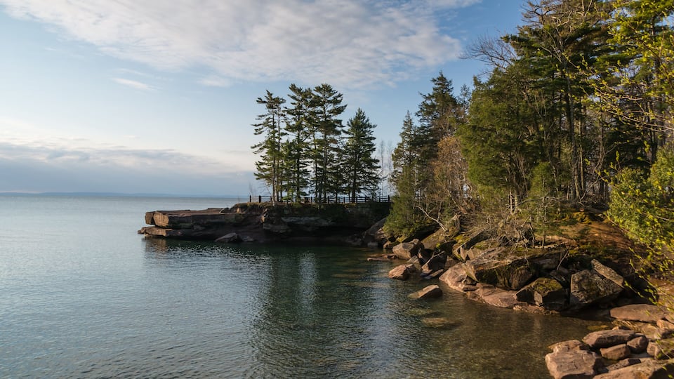 A rocky shoreline with clear water, a wooden pier, and dense forest.