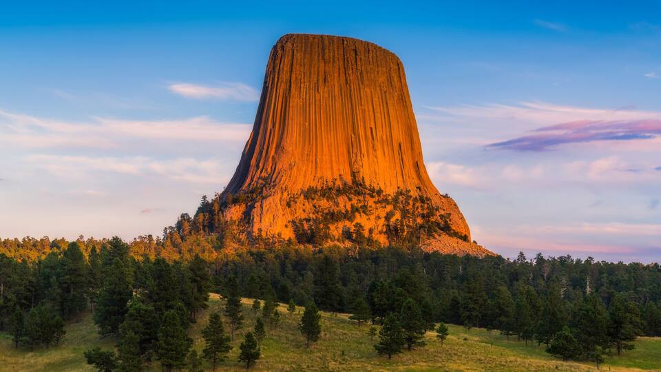 A large, steep-sided rock formation surrounded by a forested area.