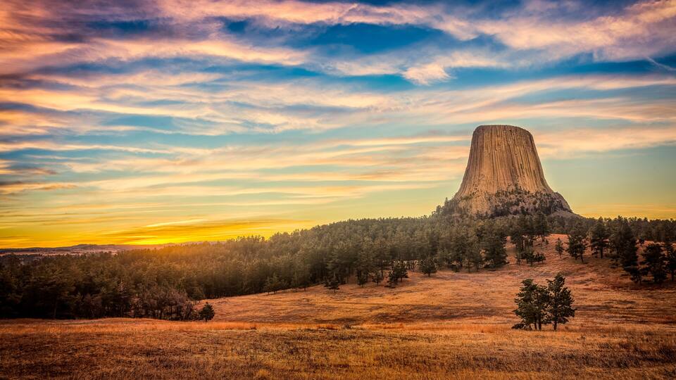 A prominent butte surrounded by a forested area with a sunset in the background.