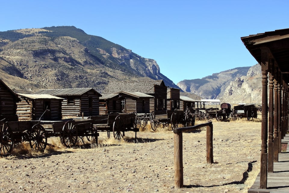 A rustic wooden building with a dirt ground and a mountain in the background.