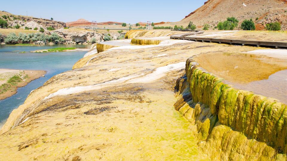 A river with a rocky, yellowish bank and a bridge in the background.
