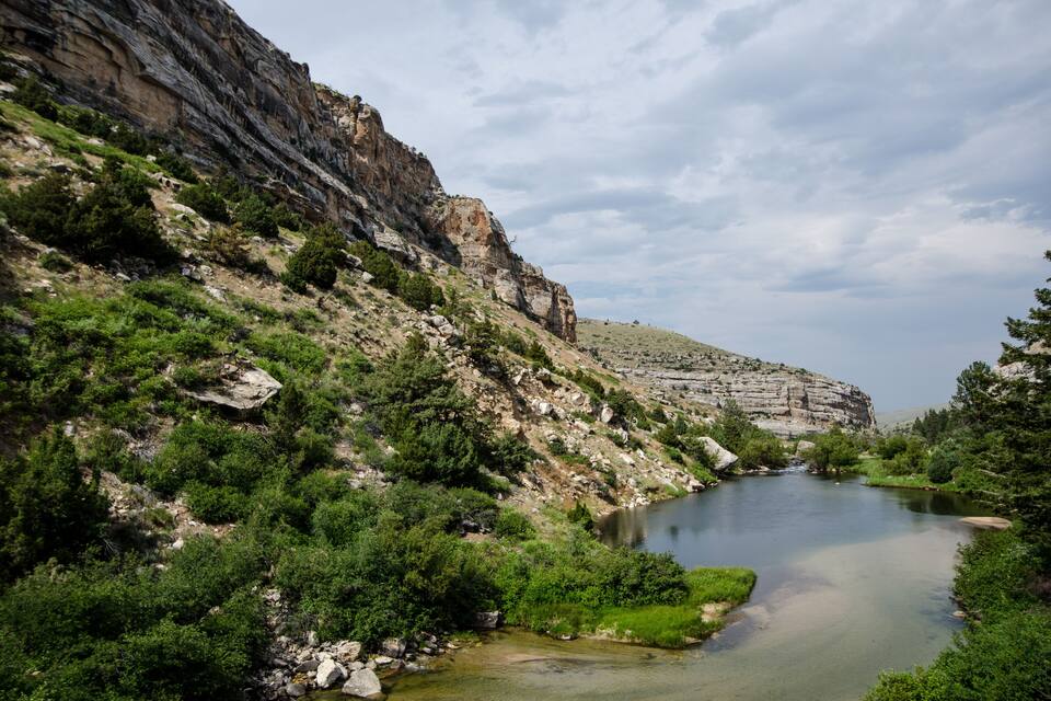 A river flowing through a rocky canyon with green vegetation and cliffs.