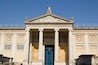 A classical building with a blue door, columns, and a statue on the roof.