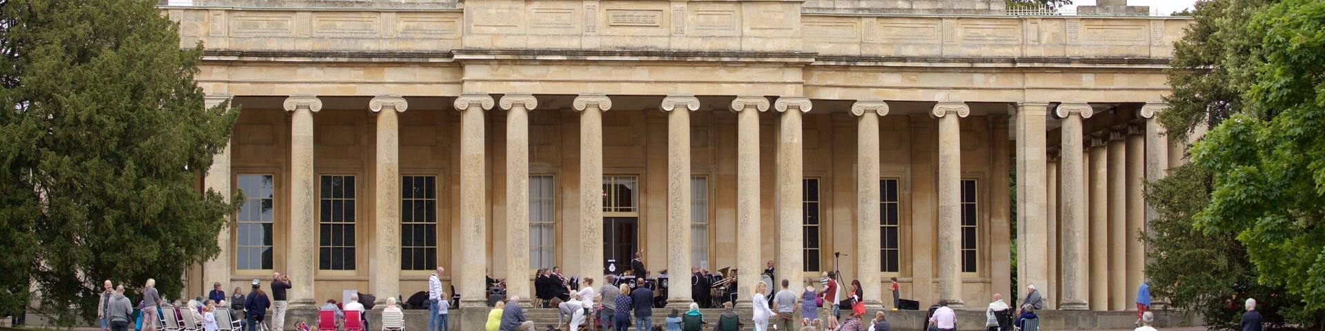 A large neoclassical building with a dome and columns, surrounded by a grassy area with people and dogs.
