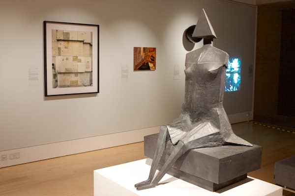 Une sculpture dans une galerie d’art, avec des œuvres encadrées accrochées au mur.