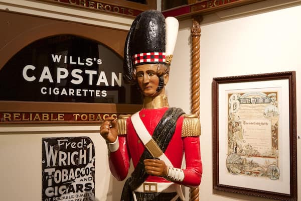 Une exposition historique comprenant une statue, une enseigne publicitaire pour les cigarettes Wills's Capstan et un document encadré.