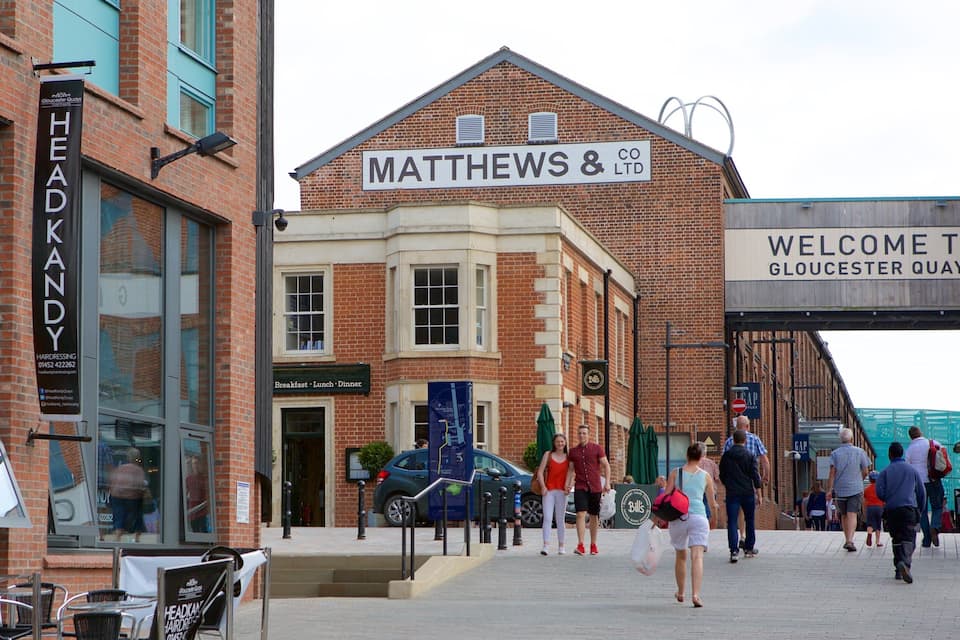 Un carrer amb un cartell de Matthews & Co. LTD, una perruxeria, i un cartell de benvinguda a Gloucester Quays.