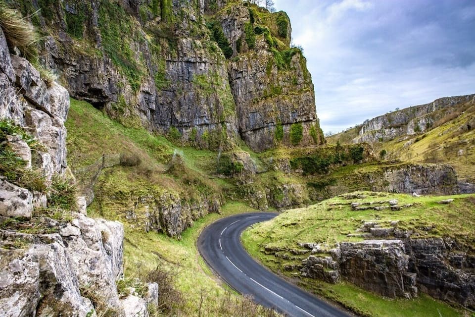 Un camino sinuoso que atraviesa un paisaje montañoso con acantilados rocosos y zonas cubiertas de hierba.