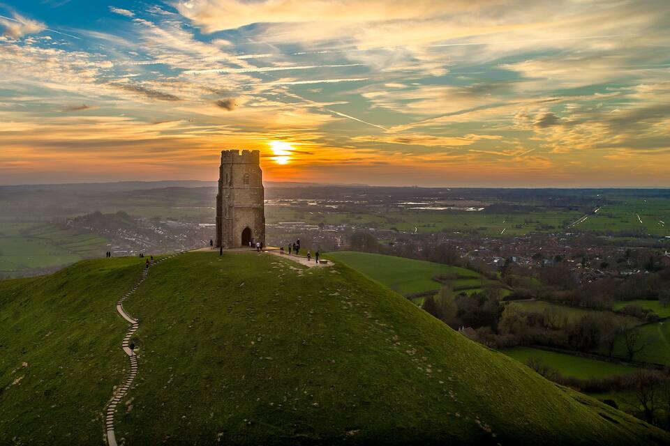 A tower on a grassy hill with a sunset in the background.