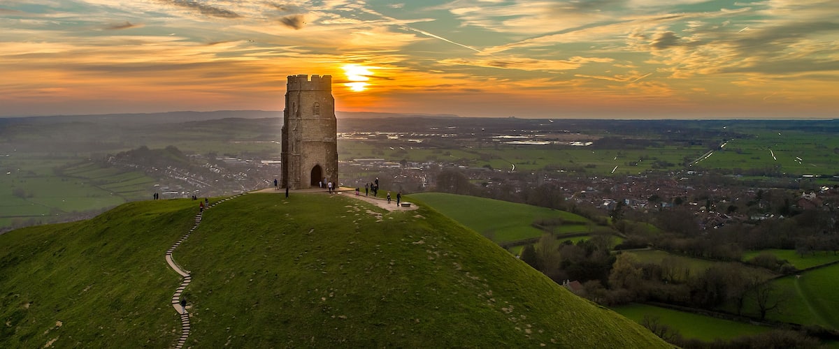 A tower on a grassy hill with a sunset in the background.