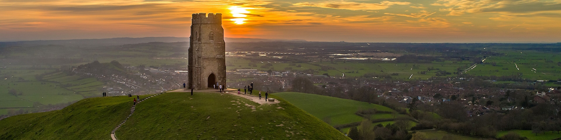 A tower on a grassy hill with a sunset in the background.