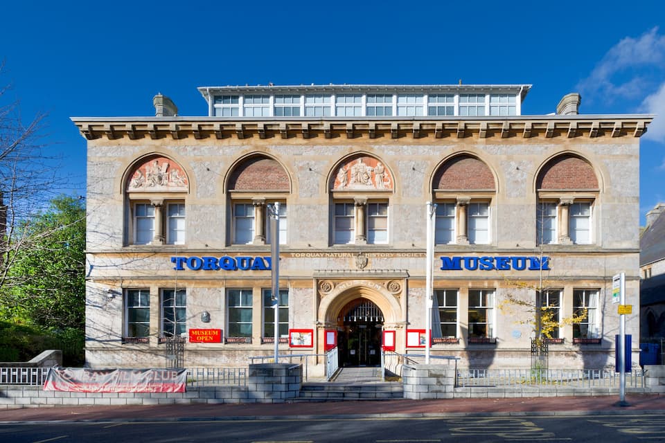 Ein historisches Gebäude mit Bogenfenstern und einem Schild, auf dem 'Torquay Museum' steht.