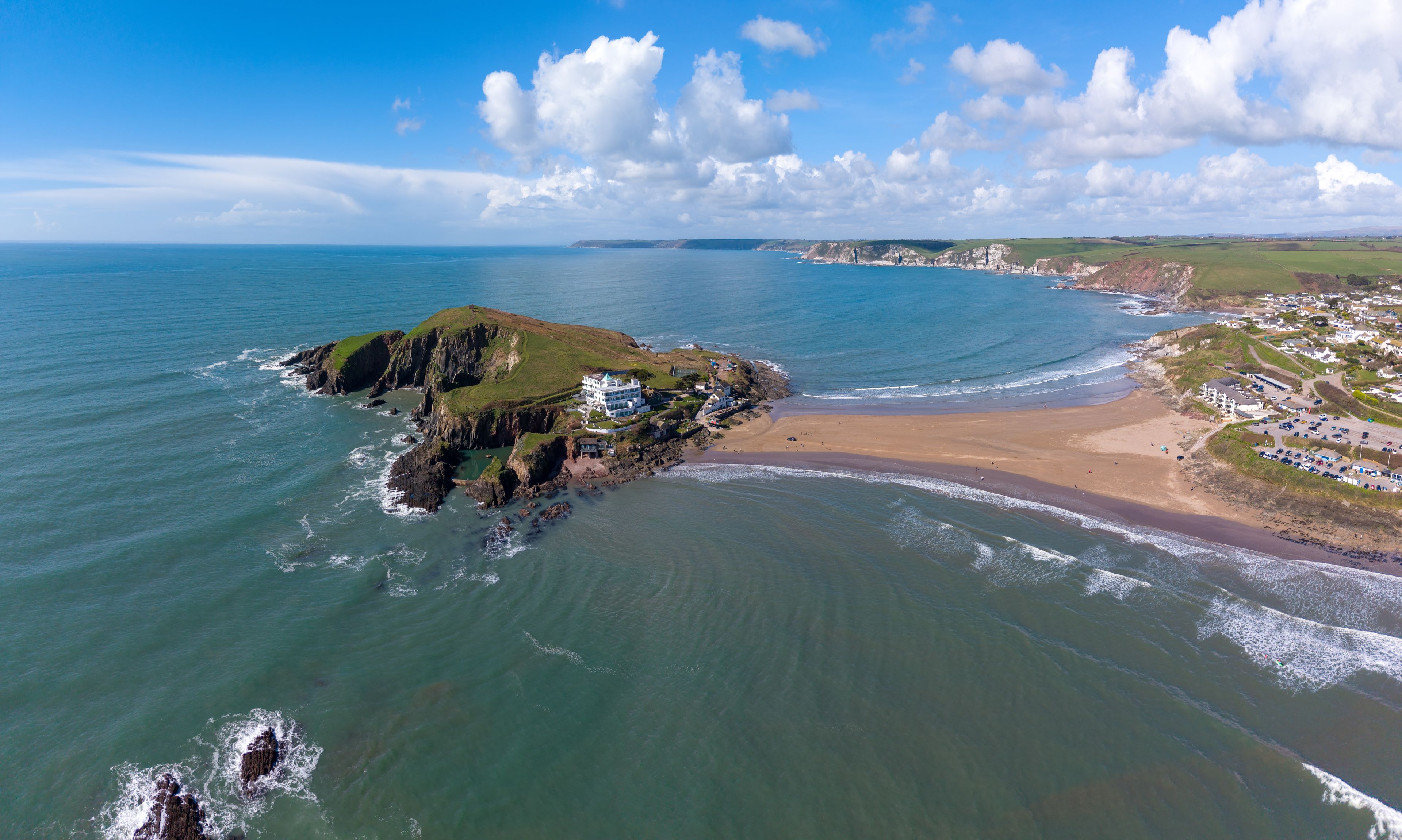 Aerial view of Burgh Island featuring the historic hotel, rocky cliffs, and sandy tidal causeway connecting to the mainland at Bigbury-on-Sea, England, United Kingdom.
