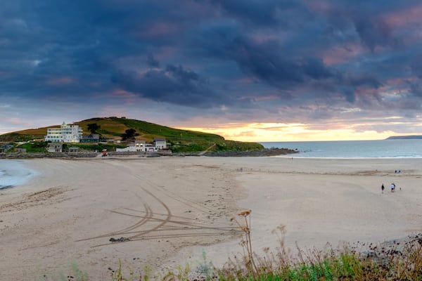 A beach with a hill, a lighthouse, and a cloudy sky.