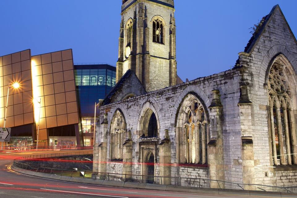 A historic church with a tall bell tower and a modern building with glass windows in the background.