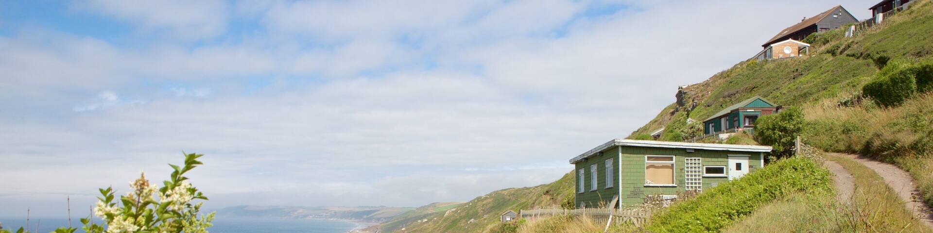 A coastal path leading to a green house on a hillside overlooking a beach.
