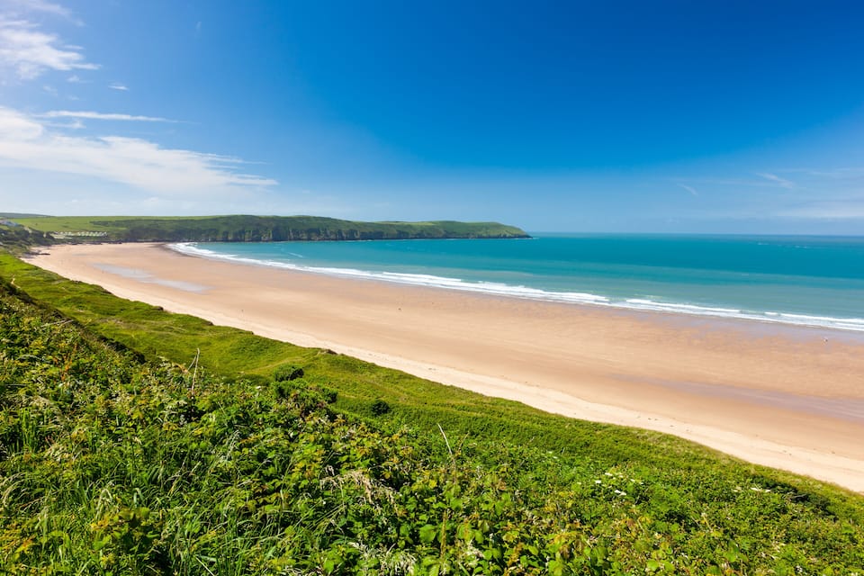 Un paysage côtier avec une plage de sable, une végétation verdoyante et un ciel bleu clair.