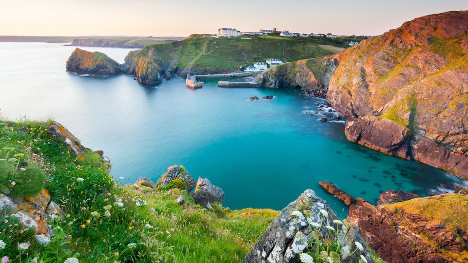 A coastal landscape with cliffs, a harbor, and a building on the hill.