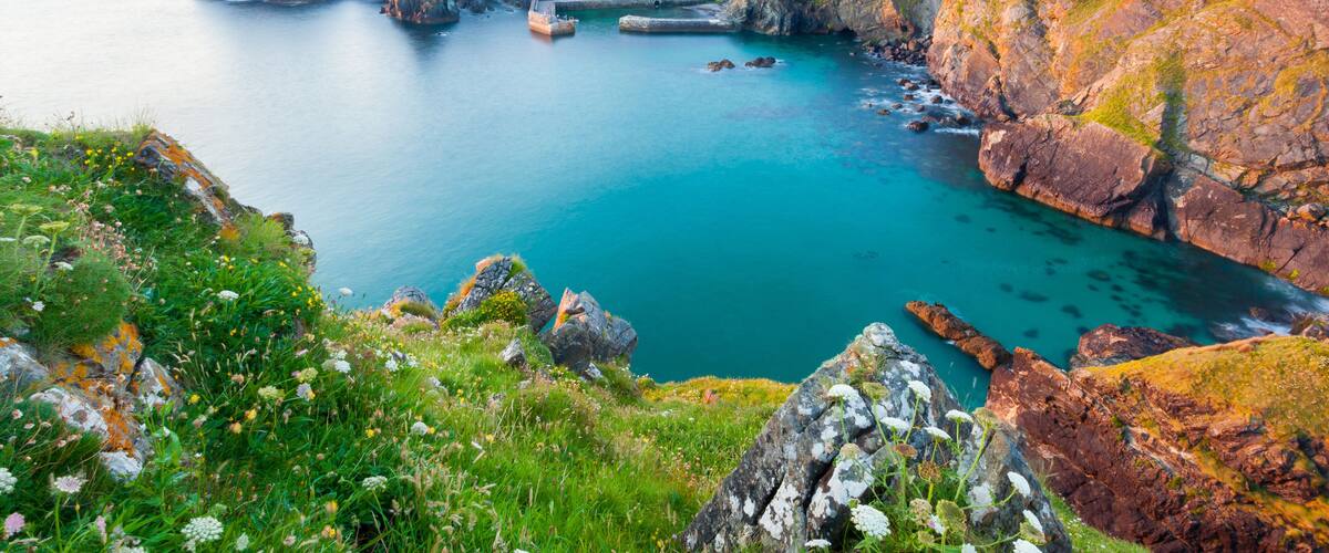 A coastal landscape with cliffs, a harbor, and a building on the hill.