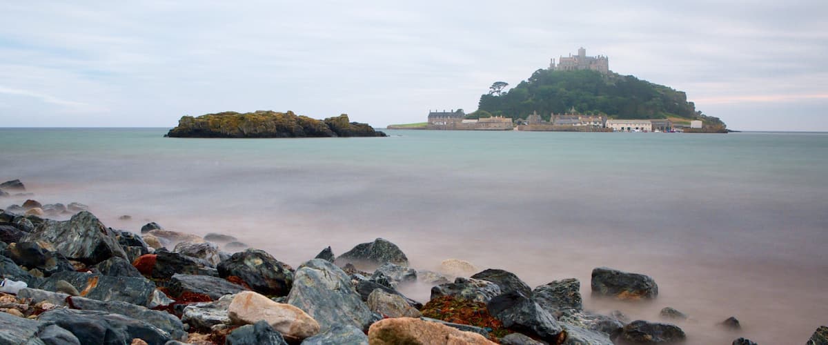 Un château perché sur une colline, dominant une mer calme et entouré de côtes rocheuses.