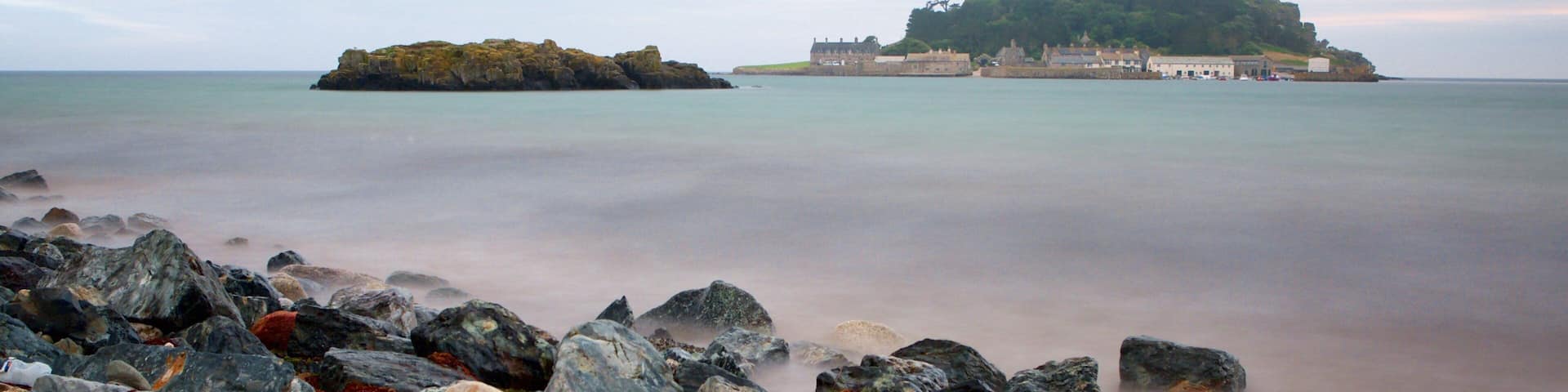 A castle on a hill overlooking a calm sea, surrounded by rocky shores.