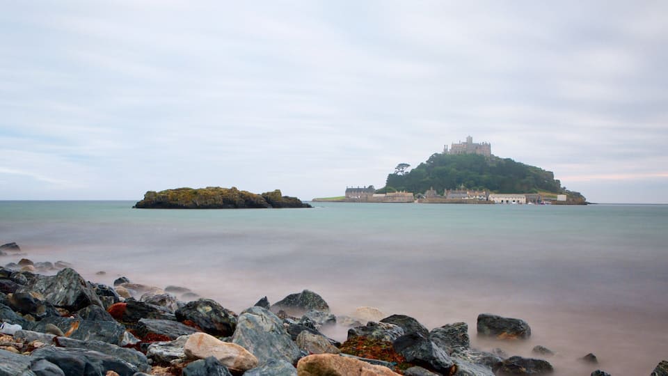 A castle on a hill overlooking a calm sea, surrounded by rocky shores.