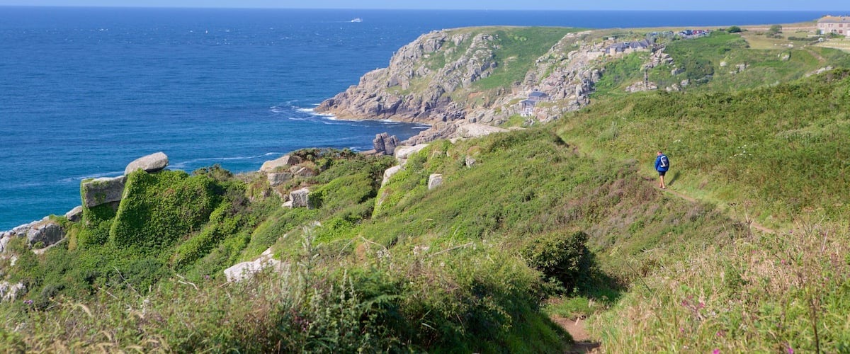 A coastal landscape with rocky cliffs, a trail, and a person hiking.