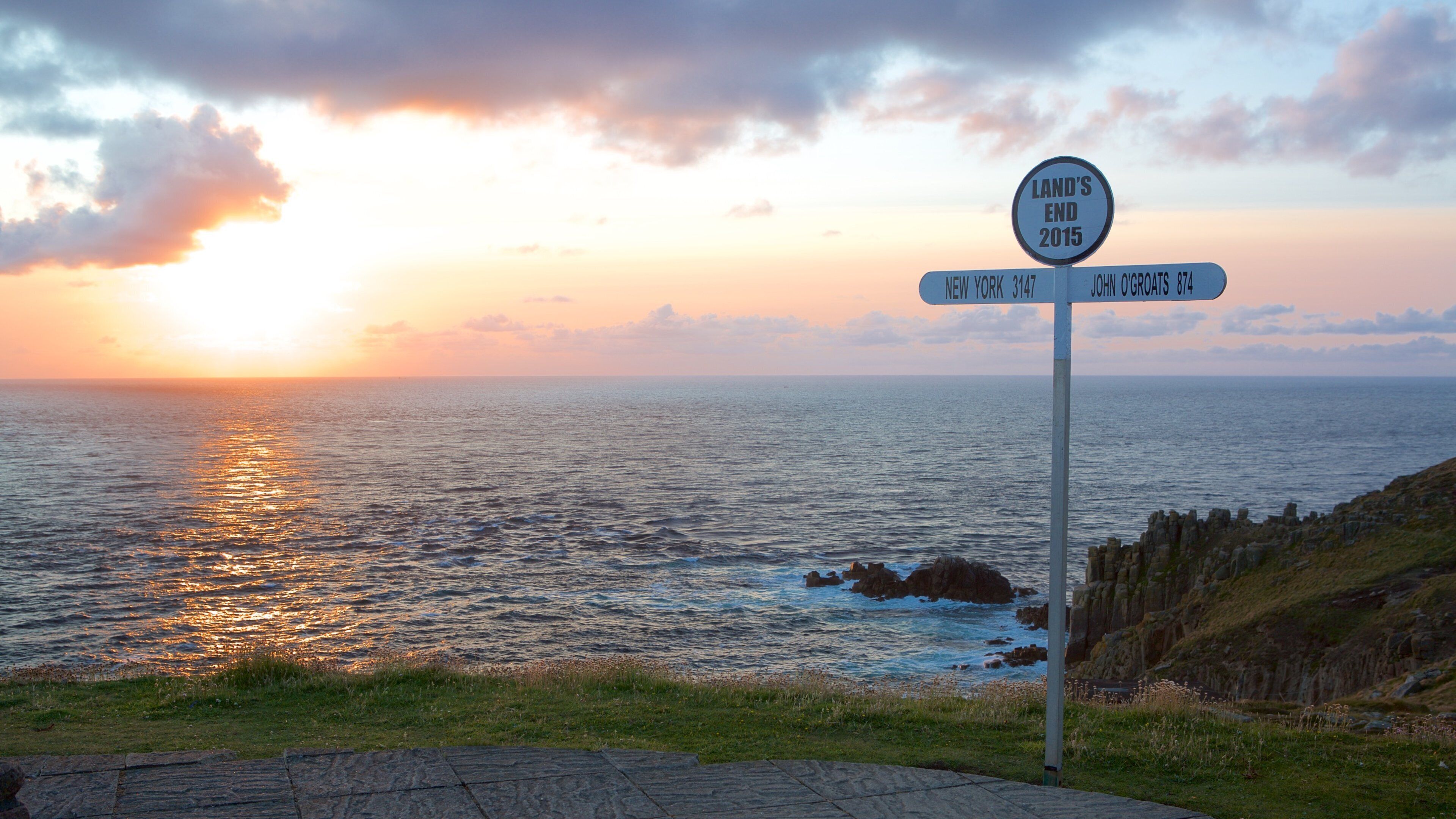 Land\'s End bevat bewegwijzering, een zonsondergang en rotsachtige kustlijn