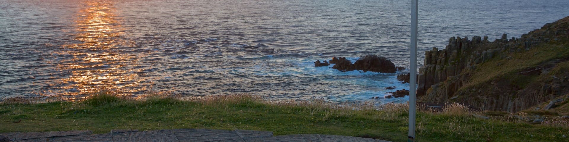 A sunset over the ocean with a sign indicating 'Land's End 2015' and directions to New York and John Ogroats.
