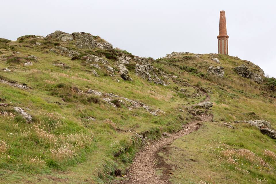A grassy hill with a stone path leading to a tall, narrow tower.