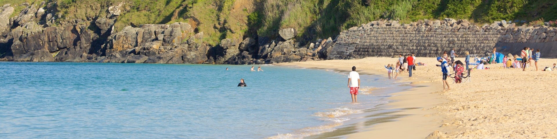 A beach with people, a rocky shoreline, and a house on a hill.