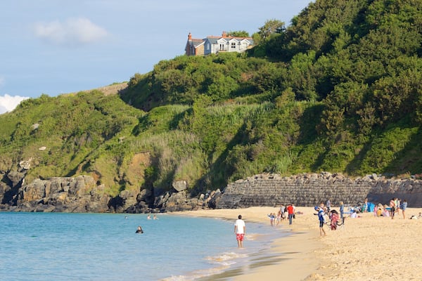 A beach with people, a rocky shoreline, and a house on a hill.